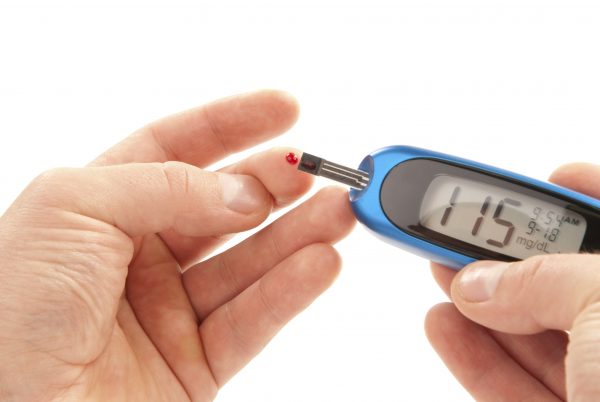 Diabetic patient doing glucose level blood test using ultra mini glucometer and small drop of blood from finger and test strips isolated on a white background. Device shows 115 mg/dL which is normal